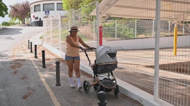 Bir kadın, bir bebek arabasını iterken banliyöde güneşli bir gün gezintisinden zevk alır. Sahne günlük yaşamın ve açık hava aktivitelerinin özünü yakalıyor..