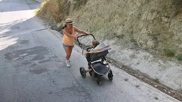 Aktif anne bebeğini bebek arabasının tepesine iterken dışarıda koşuyor. Güneşli bir gün, fitness konsepti, ebeveyn-çocuk bağı ve sağlıklı yaşam tarzı..