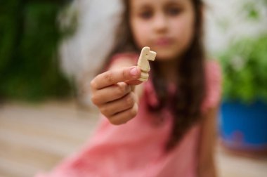 Pembe elbiseli genç bir kızın bulanık görüntüsü, elinde tahta oyuncak bir atı yeşil arka planda kameraya doğru gösteriyor..