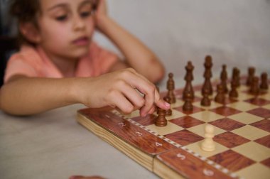 Genç bir kız satranç oyununa derinden odaklanır, satranç tahtasının bir parçasını hareket ettirir, stratejisini ve konsantrasyonunu gösterir..