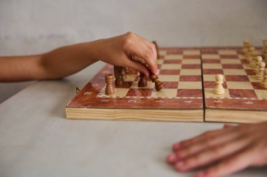 Ahşap bir satranç tahtasında satranç oynayan iki elin yakın çekimi. Parçalara ve tahtaya odaklanmış stratejik bir an..