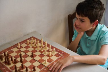 Genç bir çocuk masada oturuyor, dikkatle satranç oynuyor, odak ve stratejik düşüncelerini sergiliyor..