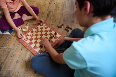 Çocuklar ahşap bir zeminde satranç oynuyorlar. Stratejik masa oyunu kritik düşünce ve zihinsel becerileri teşvik ediyor. Günlük ve eğlenceli iç etkinlik.