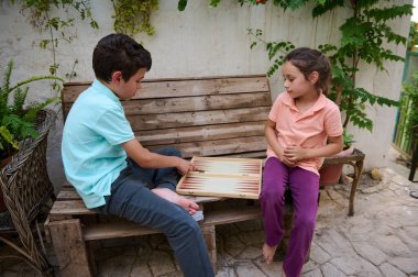 Çocuklar, yeşilliklerle çevrili ahşap bir bankta tavla oynamaktan hoşlanırlar. Boş zamanların, çocukluğun ve bağlanmanın mükemmel bir görüntüsü..