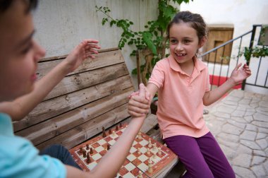 Genç bir kız, açık havada satranç oynayıp arkadaşlığını ve eğlencesini kutlayan bir arkadaşıyla mutlu bir şekilde tokalaşıyor..