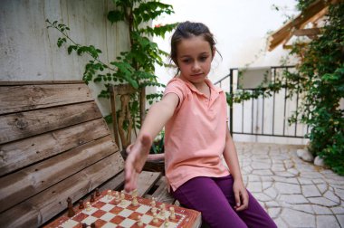 Genç bir kız dışarıda satranç oynuyor, bir sonraki hamlesini derinden düşünüyor. Bahçe düzenlemesi odaklanmasını ve konsantrasyonunu arttırıyor..