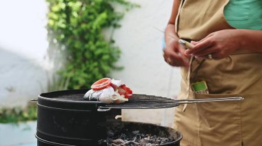Güneşli bir bahçede önlüklü biri tarafından hazırlanmış balık, domates ve soğanlı ızgaranın yakın çekimi. Mükemmel yaz yemeği konsepti..