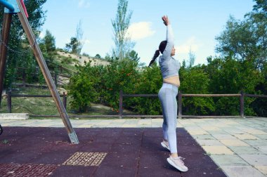 Parkta egzersiz yapan, spor kıyafetlerini giyen, dışarıda huzurlu bir ortamda sağlıklı bir yaşam tarzını ve uygunluğu teşvik eden bir kadın..