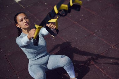 Kararlı bir kadın açık havada direnç bantlarıyla egzersiz yapıyor. Gücü ve zindeliği vurguluyor. Aktif giyinmiş, egzersiz rutinine odaklanmış..