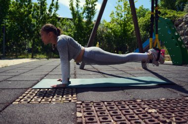 Bir kadın açık havada TRX kalas egzersizi yapıyor, açık gökyüzünün altındaki bir parkta güç ve uygunluğu vurguluyor. Zindelik ve sağlıklı yaşam tarzı kavramları için mükemmel..