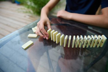 Bir el cam bir masa üzerinde domino etkisi başlatır, sakin bir açık havada hareket ve beklenti gösterir.