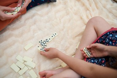 Çocuklar tüylü bir halıda domino oynuyorlar. Stratejiyi, oyunculuğu ve kapalı alanlarda kaliteli bağ kurma zamanını vurguluyorlar..