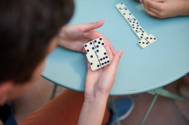 Mavi bir masada, rahat bir ortamda rahatlık, strateji ve sosyal etkileşimi gösteren bir oyun sırasında eller domino taşlarını tutar..