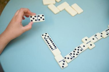 Bir el mavi bir masada domino taşını alır, klasik bir masa üstü oyununda strateji ve eğlencenin özünü yakalar..