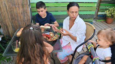 Avluda sıradan bir aile yemeği yemek, birlikte yemek yemek ve birlikte vakit geçirmek. Yetişkinler ve çocuklar rahat ve açık havada yemek ve sohbetin tadını çıkarırlar..