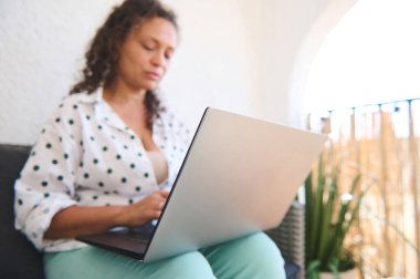 Bir kadın balkonda rahatça oturup dizüstü bilgisayarıyla çalışıyor. Rahat atmosfer, uzak bir çalışma ve sıradan bir yaşam tarzını vurguluyor..