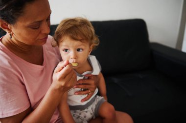Bir kadının bebeğini nazikçe beslediği, aile ortamındaki sıcaklığı ve bakımı vurguladığı dokunaklı bir sahne..