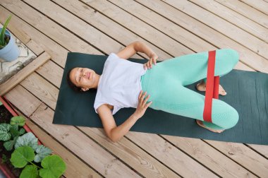 Kadın dışarıda yoga minderinde direnç bandı egzersizi yapıyor fitness ve kas güçlendirmeye odaklanıyor. Aktif yaşam tarzı ve refahı desteklemek için ideal.