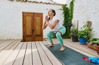 Tahta bir güvertede yoga pozu veren bir kadın, yemyeşil yemyeşil sakin bir ortamda dengeyi ve esnekliği arttırıyor..