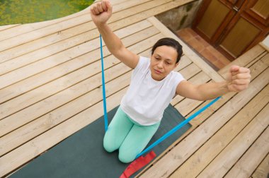 Bir kadın, açık havada yoga minderinde direniş bandı kullanarak egzersiz yapıyor, dayanıklılığını ve sağlığını arttırıyor..