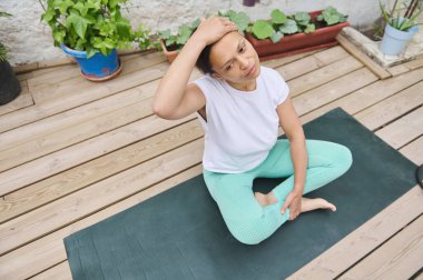 Güvertede bitkilerle yoga yapan bir kadın bahçe ortamında rahatlama ve farkındalığı teşvik ediyor..