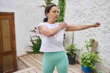 Bir kadın, sakin bir açık hava ortamında kollarını esneterek spor giysileri giyer, rahatlama ve zindelik duygusunu arttırır..