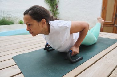 Bir kadın yoga minderinin üzerinde şınav çekiyordu. Huzurlu bir arka bahçede zindelik ve gücü kucaklıyordu..