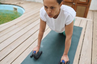 Odaklanmış bir kadın açık hava ortamında yoga minderinde şınav çekiyor. Güç antrenmanı ve fitness 'i vurguluyor..