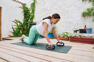 Kadın yoga minderinde, açık hava ortamında şınav çekerek spor yapıyor. Formunu, gücünü ve sağlıklı bir yaşam tarzını destekliyor..