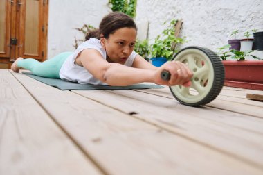 Yoga minderiyle çalışan odaklanmış bir kadın doğal ortamda zindelik, kararlılık ve kuvvete vurgu yapıyor..