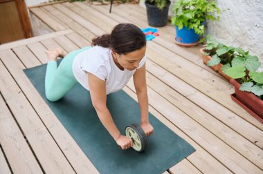 Yoga minderinde kas silindiri kullanan odaklanmış bir kadın. Sakinleştirici bir bahçe ortamında spor ve çekirdek dayanıklılığını vurgular.