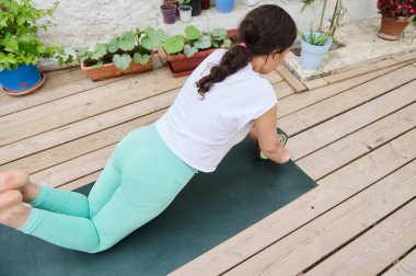 Kadın açık havada yeşil bir paspasla yoga yapıyor. Bahçe düzenlemesi, yemyeşil bitkilerle çevrili rahatlama ve zindelik odağı sağlar..