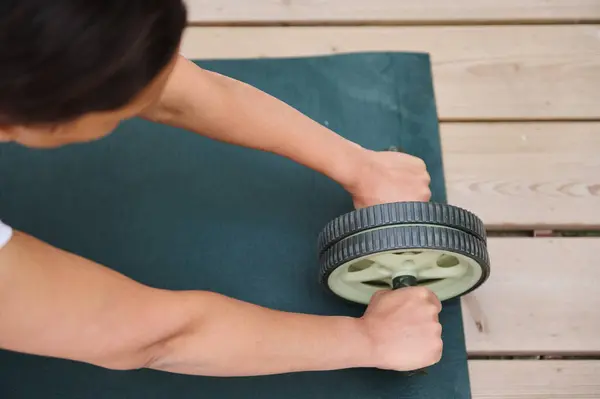 stock image A person uses an ab roller on a yoga mat outdoors, focusing on core strength and fitness. The setting evokes a sense of health, determination, and dedication to exercise.