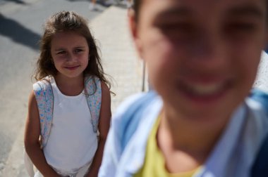 Güneşli bir günde ön planda bulanık bir insanla sırt çantasıyla dışarıda duran genç bir kız..