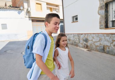 Gülümseyen kardeşler aydınlık bir günde birlikte yürürler, arkadaşlıklarının keyfini çıkarırlar. Çocuk bir sırt çantası taşıyor, sıradan bir gezintiye ya da okul gününe benziyor..