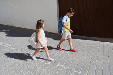 Genç bir kız ve oğlan sırt çantalarıyla bir cadde boyunca yürürler, okula giderler. Sahne güneşli bir günü ve günlük rutini yakalar..