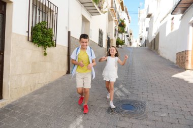 İki neşeli çocuk kaldırım taşından bir caddede koşuşturuyor, resimli bir mahallede mutluluğu ve çocukluk özgürlüğünü yakalıyorlar..