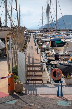 Açık mavi gökyüzünün altındaki ahşap bir rıhtıma bağlı sayısız yat ve teknenin sergilendiği, huzur ve deniz macerasının somutlaştığı pitoresk bir marina..