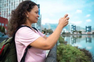 Sırt çantalı bir kadın. Rıhtımda modern bir şehir manzarası. Güneşli bir günde huzurlu bir şehir güzelini yakalıyor..