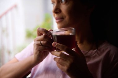 Çayı yudumlarken düşünceli bir şekilde bakan bir kadın, sakin ve düşünceli bir anı içeride yakalıyor..