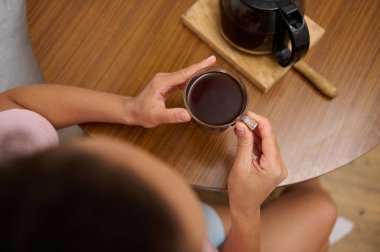 Ellerin sıcak bir fincan kahveyi ahşap bir masada tutması rahatlık ve rahatlama hissi uyandırıyor. Sabah kavramları, rahatlama ve rutin şeyler için ideal..