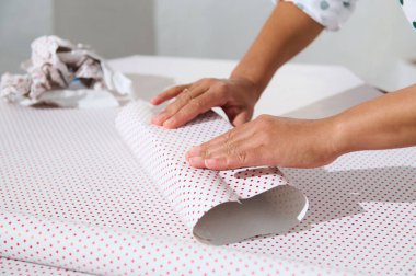 Noel hazırlığı ve yaratıcılığını gösteren bir hediyeyi puantiyeli kağıda saran ellerin yakın çekimi. Hediye ve kutlama temaları için mükemmel..