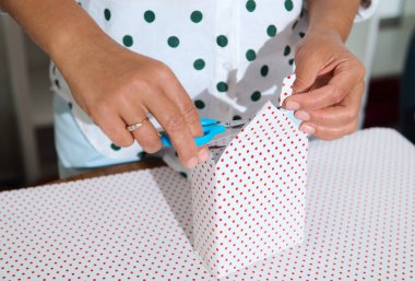 Bir insanın makas kullanarak polka kâğıdıyla hediye paketlediği yakın plan fotoğraf. Hediye verme ve festival hazırlıklarının neşe ve yaratıcılığını yakalıyor..