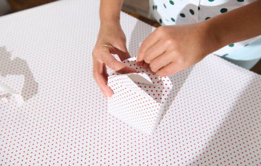 Close-up of hands wrapping a small gift box with red polka dot paper. Creative and festive decoration for special occasions. clipart