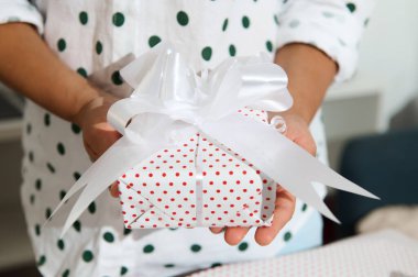 Beyaz kurdeleli ve kırmızı benekli güzel paketlenmiş bir hediye kutusunu tutan birinin yakın çekimi. Kutlamalar ve özel günler için mükemmel..