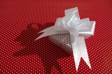 Beyaz kurdeleli güzel paketlenmiş bir hediye kutusu canlı kırmızı bir benekli arka planda duruyor, neşeli ve kutlama havası yayıyor..