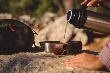 Yürüyüş sırasında, ahşap bardaklara dökülen kahvenin yakın çekimi, açık hava macerası görüntüsü..