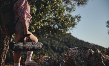 Bir yürüyüşçü, yemyeşil ormanlarla çevrili yoga minderini taşıyan kayalık bir patikada durur. Sahne, doğa macerasının ve farkındalığın özünü yakalıyor..