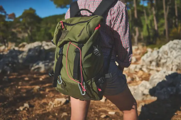 Yeşil bir sırt çantası takmış orman yolunda yürüyüş yapan biri. Açık hava, doğa, macera.