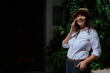 Şapka takan neşeli bir kadın dışarıda telefonuyla konuşuyor. O yemyeşil bir bahçede dururken güneş onun üzerine parlıyor. Mutluluk ve sükuneti taşıyor..